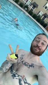 Axton shirtless in the pool holding a yellow vape. With his sister in the background, caught in a moment that makes it look like she can't swim