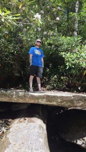 Axton in blue sliding rock shier, black shorts standing on a rock cave on Living Waters Ministry's property in WNC