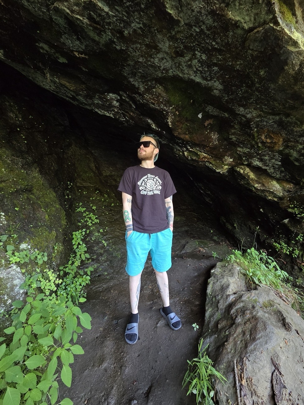 Axton in gray shirt, blue shorts and standing in a cave by the road.