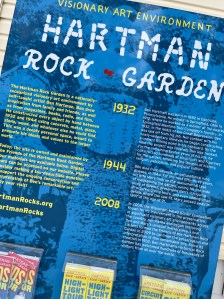 Blue sign with yellow font explaining the history of the Hartman rock garden