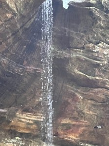 Water falling over sandstone cliffs edge looking up and over from below, sunlight catches in tge falling water 